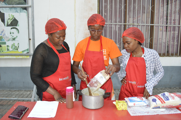 Three women preparing food together, with a Mina Lawe magazine